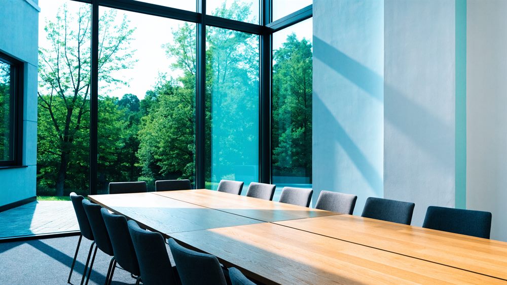 Moderner Besprechungsraum mit langem Eichentisch vor bodentiefer Verglasung ins Grüne